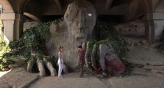 two people are standing in front of a giant stone statue with vines growing on it