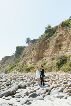 a man and woman are standing on rocks near the ocean with cliffs in the background