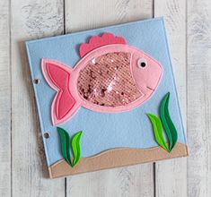 a card with a pink fish and green leaves on the front, sitting on a white wooden surface