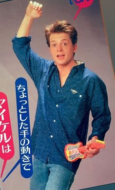 a young man in blue shirt and jeans holding an orange object with both hands while standing next to a sign