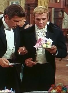 two men in tuxedos looking at something on a plate while another man looks down