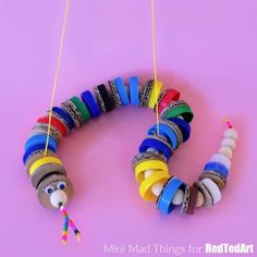 a colorful bead necklace hanging from strings on a pink background