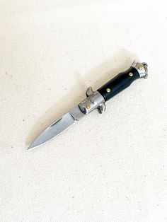 a knife that is on top of a white surface with a black handle and gold rivets