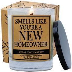 a candle that is sitting in front of a box with the words smells like you're a new homeowner on it