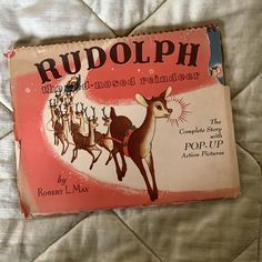 an old children's book about rudolph is laying on a bed with white sheets