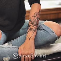 a woman with a rose tattoo on her arm sitting on the floor next to a window