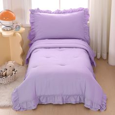 a purple bed with ruffles and pillows in a room next to a window