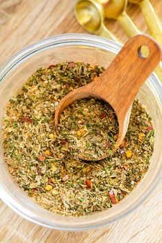 a wooden spoon in a glass bowl filled with various herbs and spices on a table