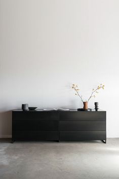 two vases with flowers sit on top of a black cabinet in front of a white wall