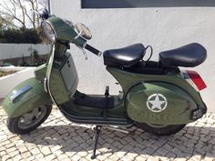 a green scooter parked in front of a white building on cobblestone