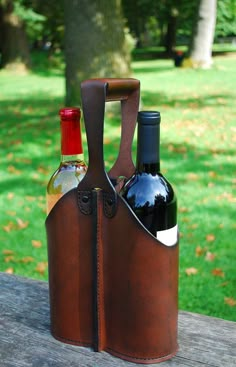 two bottles of wine sit in a leather carrier on a picnic table with green grass