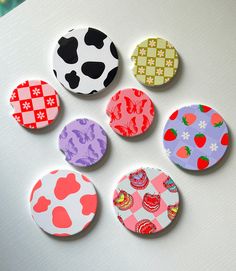 six buttons with different designs on them sitting on top of a white surface and one has an apple