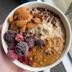 a hand holding a bowl filled with different types of food and nuts on top of it