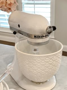 a white kitchen mixer sitting on top of a counter next to a flower vase with pink flowers in it