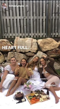 four women sitting on a blanket with food and drinks in front of them that says heart full