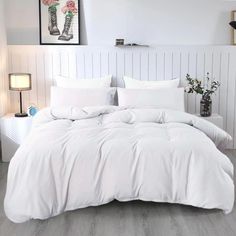 a bed with white comforter and pillows in a room next to a painting on the wall