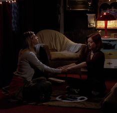 two women are sitting on the floor in front of a couch and one is holding her hand out