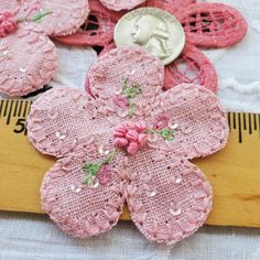 some pink flowers are next to a measuring tape and a dime on a tablecloth