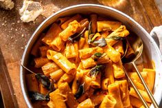 a bowl filled with pasta and spinach on top of a wooden table next to silverware