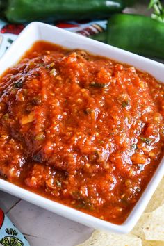 a white bowl filled with salsa next to tortilla chips and jalapenos