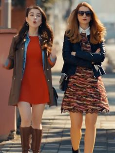 two young women walking down the street with their arms crossed and looking at each other