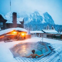 a woman in a hot tub on top of a snow covered roof next to a mountain