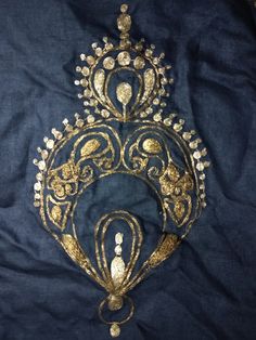 an ornate gold and blue piece of art on a dark blue cloth with white beads