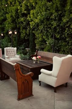 a wooden table with chairs around it in the middle of a patio area surrounded by greenery