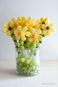 a vase filled with yellow flowers and green grapes