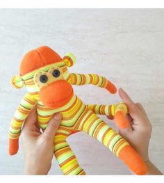 a person holding a stuffed animal in front of a white wall with an orange and yellow striped sock monkey