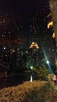 people are sitting on benches near the water at night in new york city's financial district