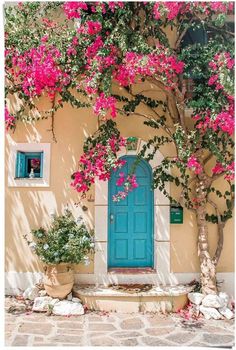 a blue door surrounded by pink flowers on a building with stone steps and trees in front