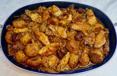 a blue bowl filled with cooked chicken and brown sauce on top of a white table cloth