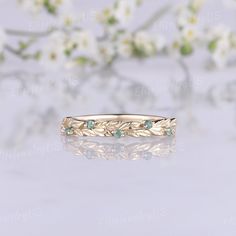 a gold ring with leaves and green stones on the side, sitting next to white flowers