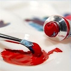 a close up of a paintbrush and red liquid on a white surface with other paints