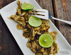 a white plate topped with chicken and limes on top of a wooden table next to a fork