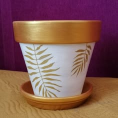 a white and gold planter sitting on top of a wooden table next to a purple wall