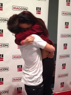 two people hugging each other in front of a wall