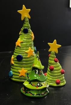 two ceramic christmas trees sitting on top of a black table next to eachother