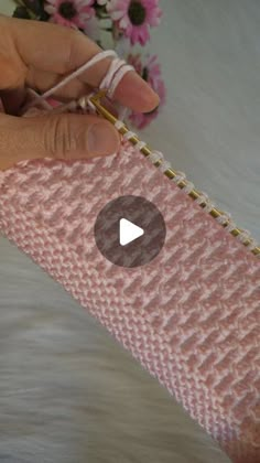 a hand holding a piece of pink knitted material with the needle pointed at it