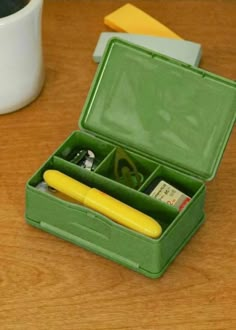 a green box with compartments holding pens and other items