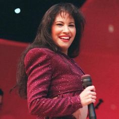 a smiling woman holding a microphone in her right hand and wearing a red jacket with sequins on it