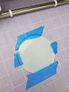 a white plate with blue tape around it sitting on a tile floor next to a ruler