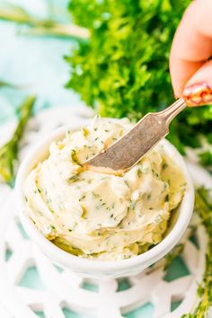 a hand holding a spoon over a bowl of dip with parsley on the side