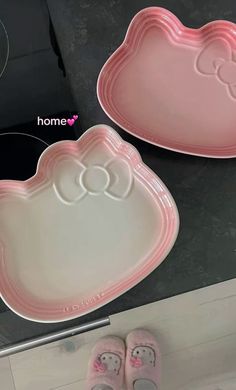 two pink trays with hello kitty designs and slippers on the floor next to each other