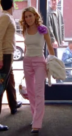 a woman in pink pants is walking down the street with her hand on her hip