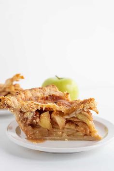 an apple pie on a white plate with some apples in the backgroung