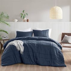 a bed with blue comforters and pillows in a room next to a plant on the floor