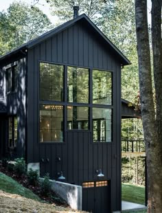 a black house with lots of windows on the front and side of it, surrounded by trees