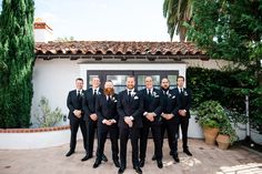 a group of men standing next to each other in front of a white building with trees